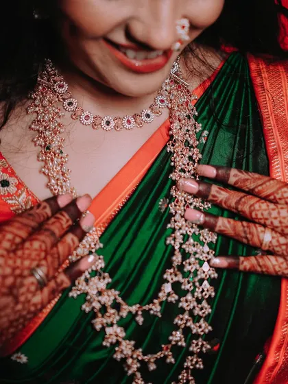 A close-up shot that puts the focus on the bride's magnificent layered necklaces and her dark green saree. This highlights the beauty and craftsmanship of traditional wedding jewellery.