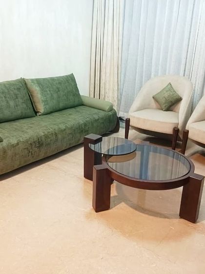 This living room set, featuring a green three-seater sofa and two cream-colored accent chairs, creates a balanced and inviting atmosphere. The simple, clean lines of the furniture are complemented by a modern multi-level center table.