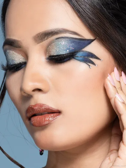 A beauty portrait with eyes closed, showing off the detail of a creative, wing-like eyeshadow design with glitter and rhinestones.