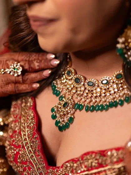 A sneak peek at the details. The emerald green jewelry provides a beautiful contrast against the red lehenga, adding a pop of color and a touch of royal elegance to the bridal look.