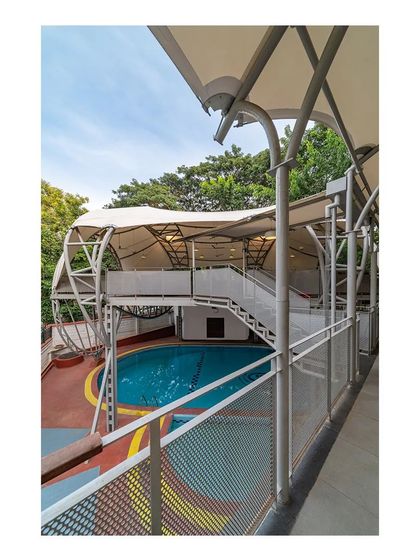 A view from an adjacent building shows how the new restaurant deck is elevated above the pool. The curved steel structure and fabric roof create a dynamic, sculptural form that has become a popular new addition to the club.