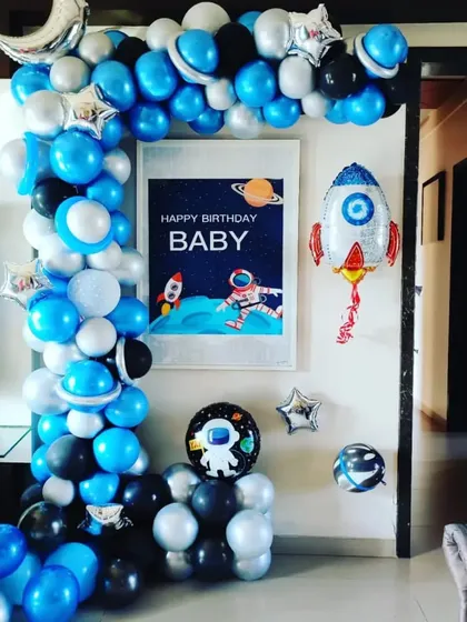 A compact yet creative space-themed birthday decoration for a home. The balloon arch in blue, black, and silver frames a "Happy Birthday Baby" poster with space graphics.