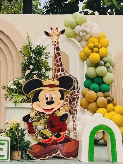 A close-up of the Mickey Mouse safari decor, showing the explorer Mickey cutout next to a tall giraffe and a balloon garland in safari-inspired colors.