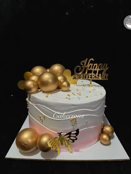 A simple yet beautiful anniversary cake. The pink and white ombre is decorated with golden spheres and butterflies, complete with a 'Happy Anniversary' topper.