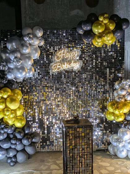 A stylish corner balloon arrangement in black, gold, and silver against a black sequin wall, creating an elegant and modern photo booth.