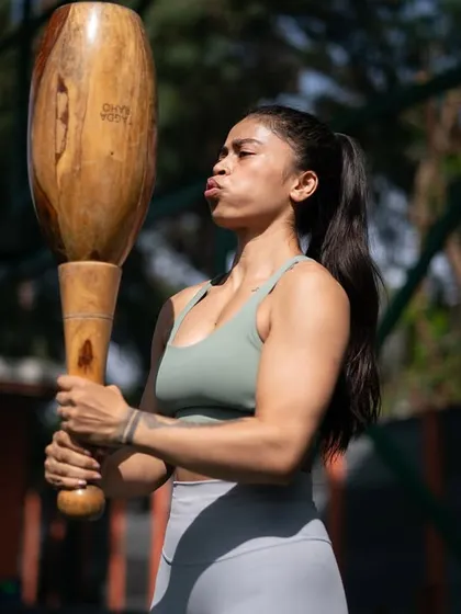 A woman powerfully lifts a Mudgar, her expression a mix of effort and determination. This shot captures the raw strength and spirit we cultivate in our sessions, inviting everyone to get fit the desi way.