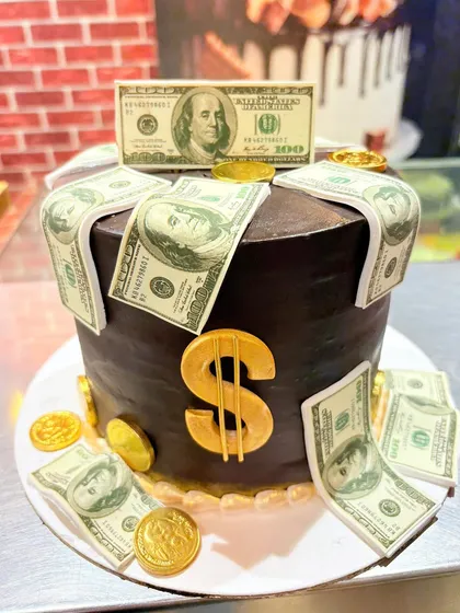 A rich chocolate cake overflowing with edible dollar bills and gold coins.