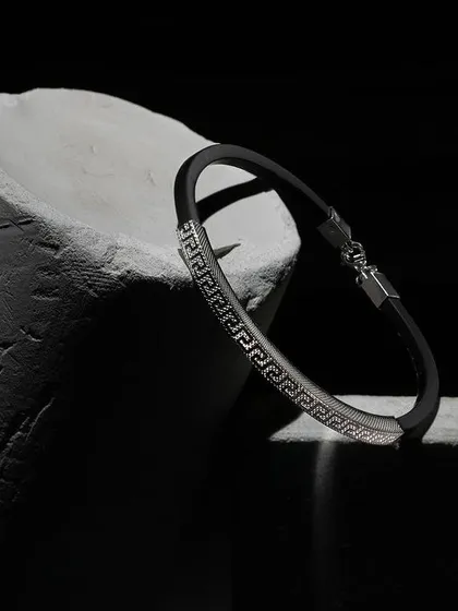 A moody shot of a men's bracelet on a rough, cylindrical stone prop. The dramatic side lighting highlights the texture of both the bracelet and the prop, creating a rugged and powerful image.