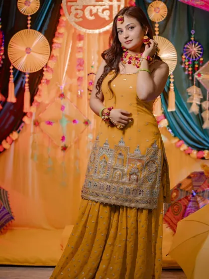 A full-length shot of bride Nidhi showcasing her beautiful yellow sharara against the festive Haldi decor. We make sure to capture the details of your outfit.