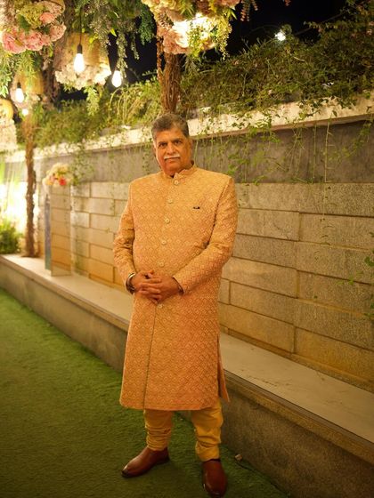 A full-length view of the golden-beige bandhgala, worn as a sherwani. Paired with a matching churidar, this is a timeless and sophisticated outfit for any wedding celebration.