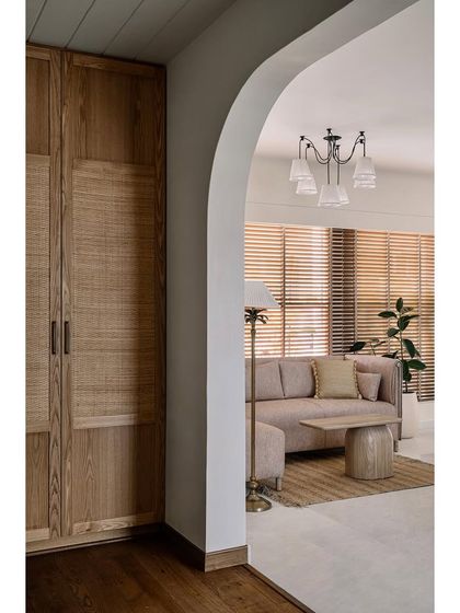 A view through an archway into the guest bedroom, showcasing the warm, cottage-inspired design with woven and wooden textures.