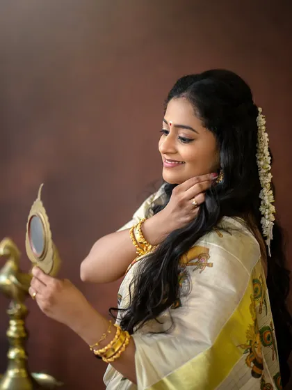 A beautiful detail shot of a mother dressed in a traditional Kerala saree, looking into an Aranmula Kannadi. These small moments of preparation are part of the story.