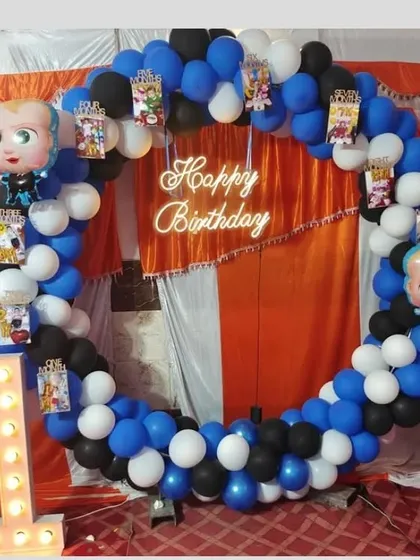 A 'Boss Baby' themed first birthday party. A circular balloon arch in blue, white, and black is decorated with character foil balloons and paired with a light-up number '1'.