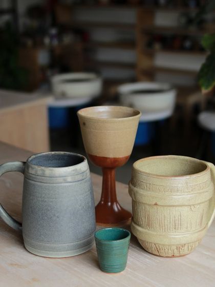 A showcase of drinkware created by our professional program students, including a large beer mug, a goblet, and a barrel shaped mug, demonstrating their skill in creating diverse and functional forms.