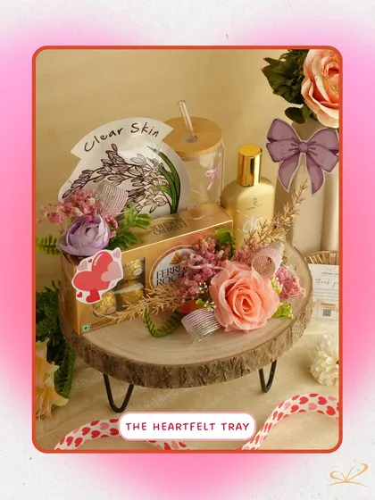 'The Heartfelt Tray' is a rustic yet elegant arrangement on a wooden platter. It features Ferrero Rocher, a glass tumbler, and a face mask, combining gourmet treats with self-care.