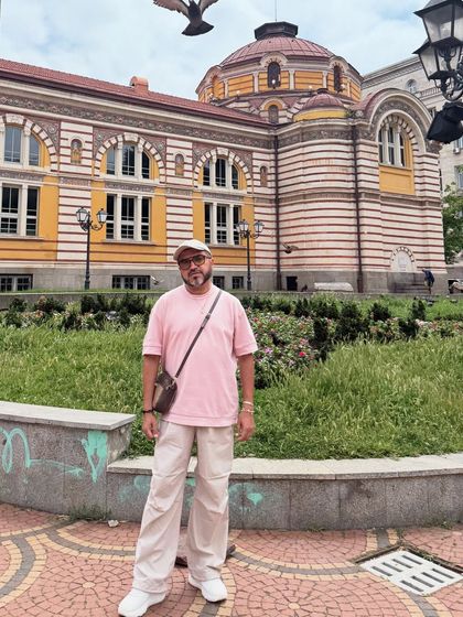 Another look from Sofia, pairing the pink tee and beige pants with a crossbody bag and cap for a relaxed, streetwear-inspired vibe.