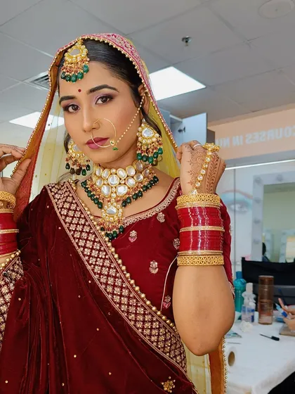 A classic bridal pose, showing off the intricate details of the velvet lehenga, kundan jewelry, and the expertly applied makeup.