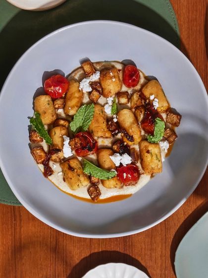 A top-down view of the pan-seared gnocchi, highlighting the vibrant colors of the blistered tomatoes and fresh mint against the creamy base.