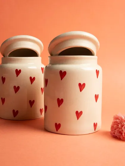 A pair of charming ceramic jars with a hand-painted red heart pattern, styled with a pink carnation.