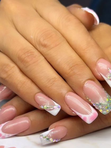 A glamorous French manicure with a twist, featuring sparkling rhinestone-covered tips and abstract pink and white patterns.