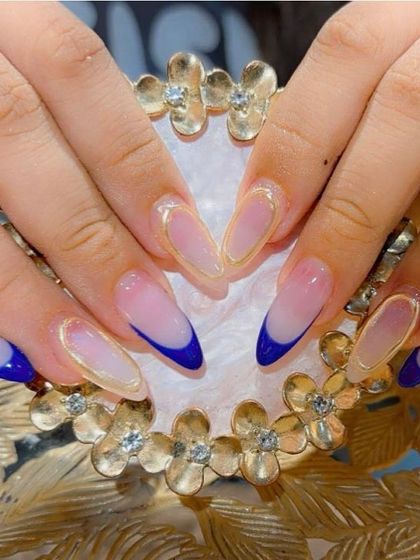 A bold and modern design with deep blue French tips outlined in gold chrome on long, pointed stiletto extensions.