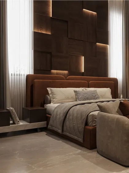 A close-up of the bed in this moody bedroom, showing the rich brown upholstered headboard and the layered bedding. The custom wood-paneled wall with integrated lighting creates a warm, ambient glow.