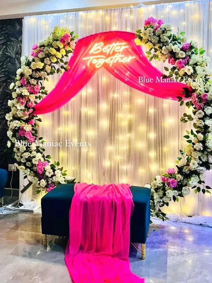 This Roka ceremony decoration uses a full floral ring with white and pink roses. The vibrant pink draping and 'Better Together' neon sign create a bold and beautiful statement piece.