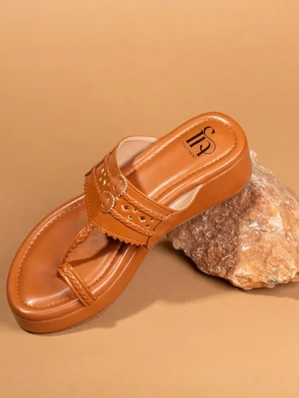 A product-only shot of a tan-colored ethnic sandal propped on a rock. The simple, earthy styling complements the design of the footwear.