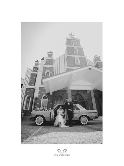 A dramatic black and white shot of the couple and their vintage car in front of the church, highlighting its grand architecture.
