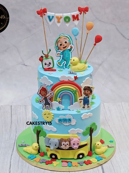 A joyful two-tier Cocomelon cake for a first birthday. This 3kg black forest cake is decorated with fondant characters, a rainbow, and a yellow school bus at the base.