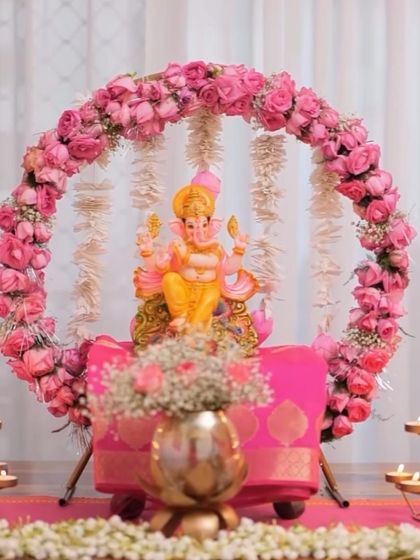 A delicate and pretty Ganpati decoration with a ring of pink roses and hanging jasmine flowers. The pink silk cloth on the pedestal completes this soft and elegant look.