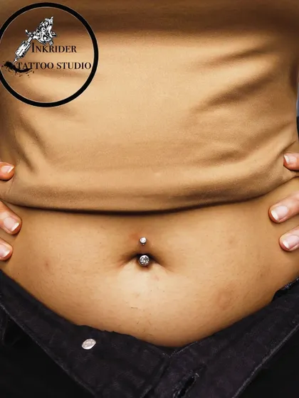 A classic navel piercing featuring a simple, elegant crystal barbell. This close-up shows the clean placement and precision I aim for with every body piercing.