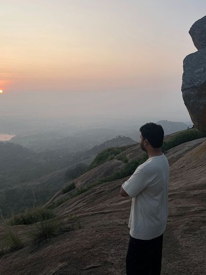 A trekker stands with arms crossed, taking in the serene sunrise view from the top of Uttari Betta.