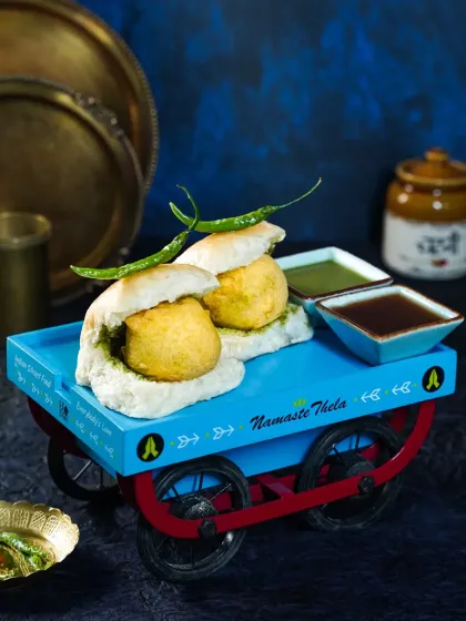 A playful shot of Vada Pav served on a miniature, brightly colored food cart (thela). This creative concept brings the energy of Mumbai's street food scene to life in a unique way.