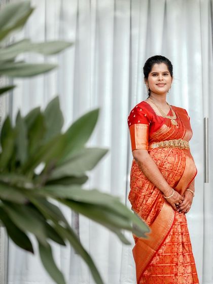 A classic full-length portrait of the expecting mother in a vibrant silk saree. The clean, modern background helps her and her traditional attire stand out beautifully.