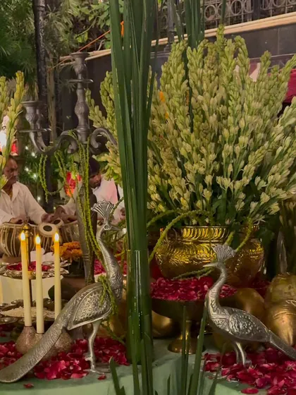 Silver peacock statues and candles are placed amongst arrangements of tuberose, adding a touch of elegance and traditional symbolism to the decor for the spiritual gathering.