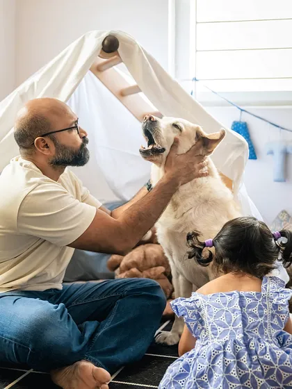 A tender moment between a father and his senior dog, Shelby, inside a play tent. The daughter looks on, showing how the family dog is central to their playtime and their lives.