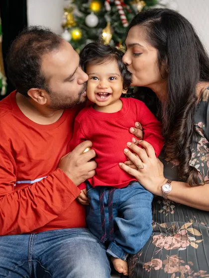 A heartwarming photo of parents kissing their smiling baby, a perfect capture of family love during Christmas.