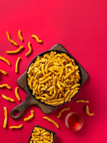 A classic Indian snack, Bhavnagri Gathiya, photographed on a striking red background for packaging. The overhead angle provides a clear and appealing view of the product.