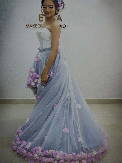A studio shot of the white and grey high-low frock. This view shows the full train, which is adorned with delicate pink flowers, adding a touch of romance.