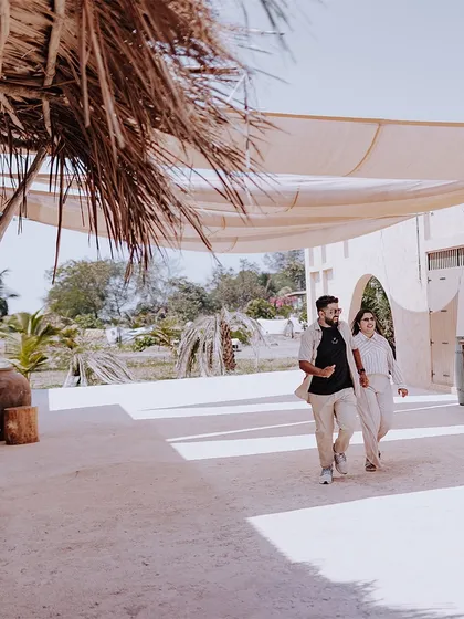 A wide shot of a couple walking hand-in-hand through a beautiful, sunlit resort, perfect for a destination pre-wedding feel.