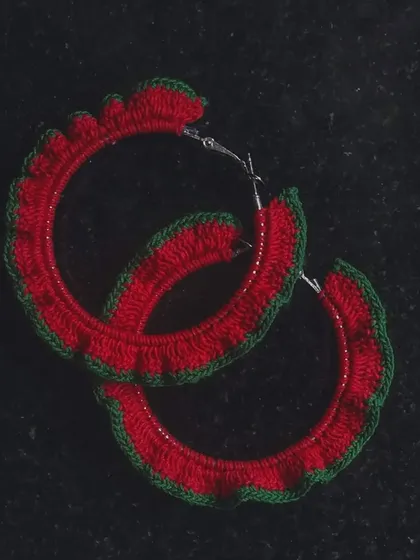These crochet hoop earrings feature a festive red and green frilly edge. They are a fun and lightweight accessory, perfect for holiday parties or adding a pop of color.