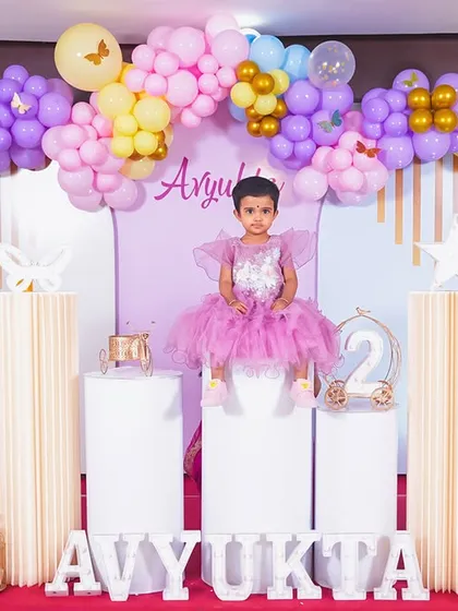 A full-length portrait of the birthday girl seated proudly amidst her party decorations.