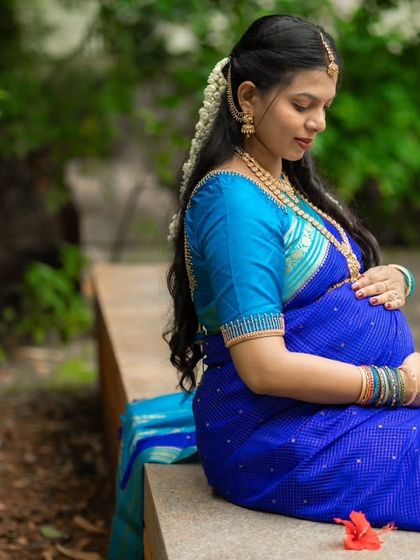 A quiet, reflective moment outdoors. Seated on a bench, this mom-to-be cradles her bump in a beautiful blue saree, surrounded by the peace of nature.