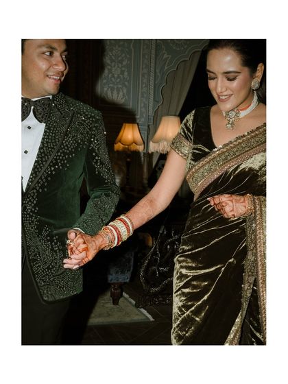 A close-up of the couple, hand in hand. The groom's embellished jacket and the bride's velvet saree are perfect for a glamorous reception look.