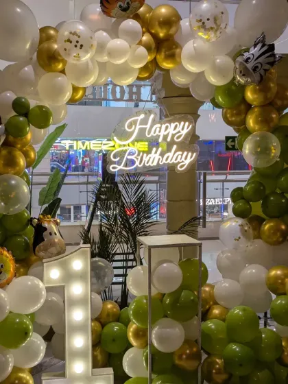 Another look at the jungle theme decor, highlighting the "Happy Birthday" neon sign nestled among the balloons and tropical leaves.