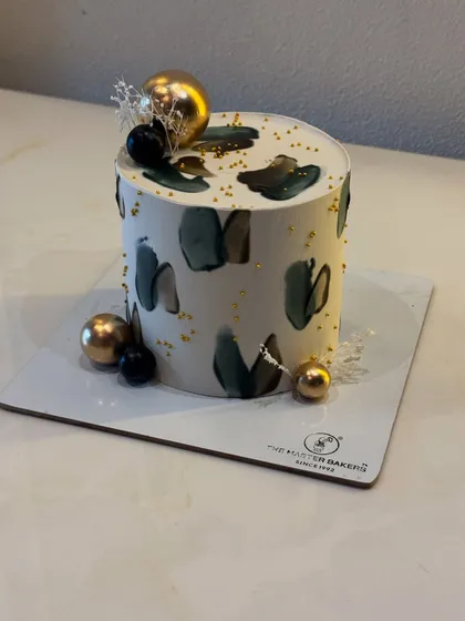 This cake showcases a modern, minimalist aesthetic with abstract buttercream strokes in muted tones. Accented with gold leaf and decorative spheres, it's a sophisticated choice for milestone birthdays, anniversaries, or any contemporary celebration.
