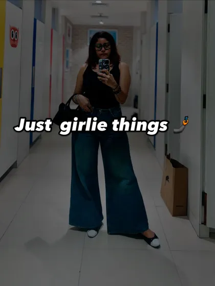 A 'just girlie things' mirror selfie in a trial room, wearing a black tank top and wide-leg jeans.