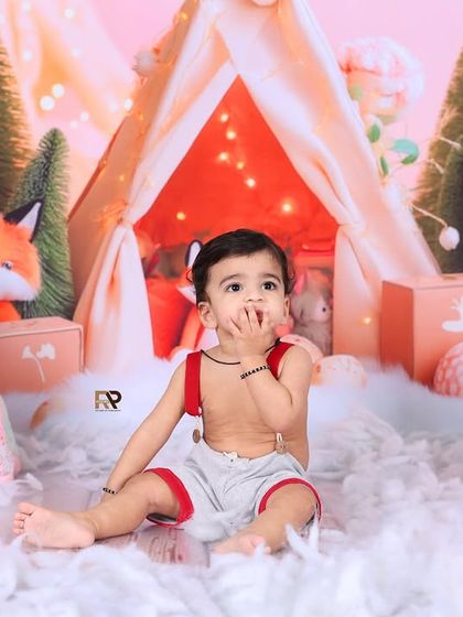 A baby boy sits amidst a snowy, fox-themed woodland scene, looking thoughtfully at the camera. The mix of textures and props creates a rich and imaginative setting.