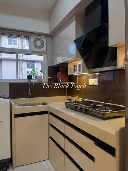 This modern kitchen features glossy white cabinets with handleless drawers and a dark, contrasting backsplash. The layout is designed for efficiency, with the sink, hob, and washing machine all neatly integrated.